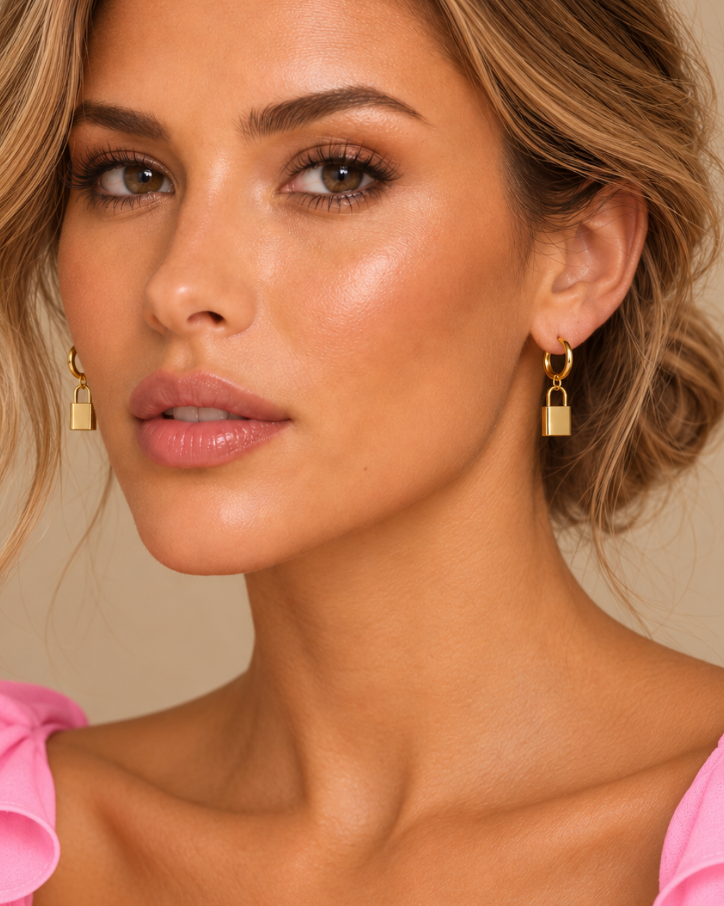 Close beauty portrait of the pink Saint Barts model wearing paired gold lock earrings with her hair in a bun.